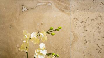 A framed abstract painting above a tiled wall with a vase of white orchids.