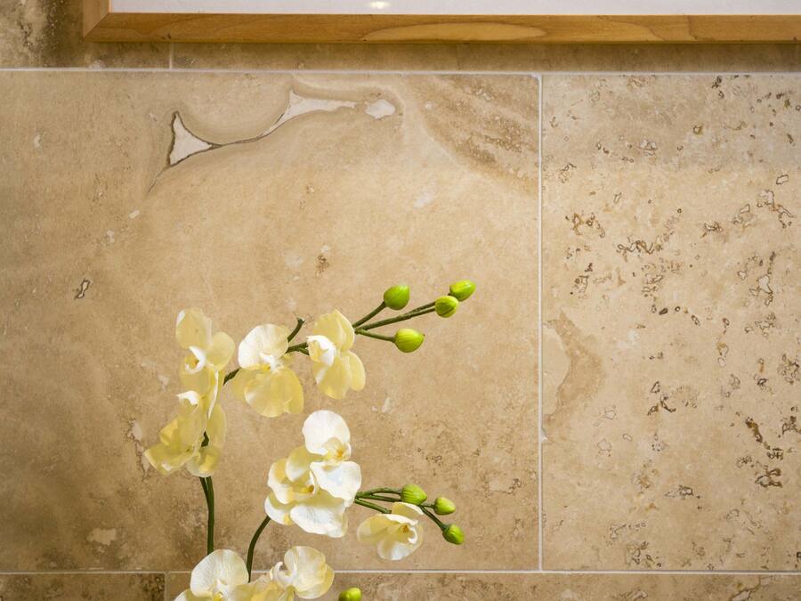 A framed abstract painting above a tiled wall with a vase of white orchids.