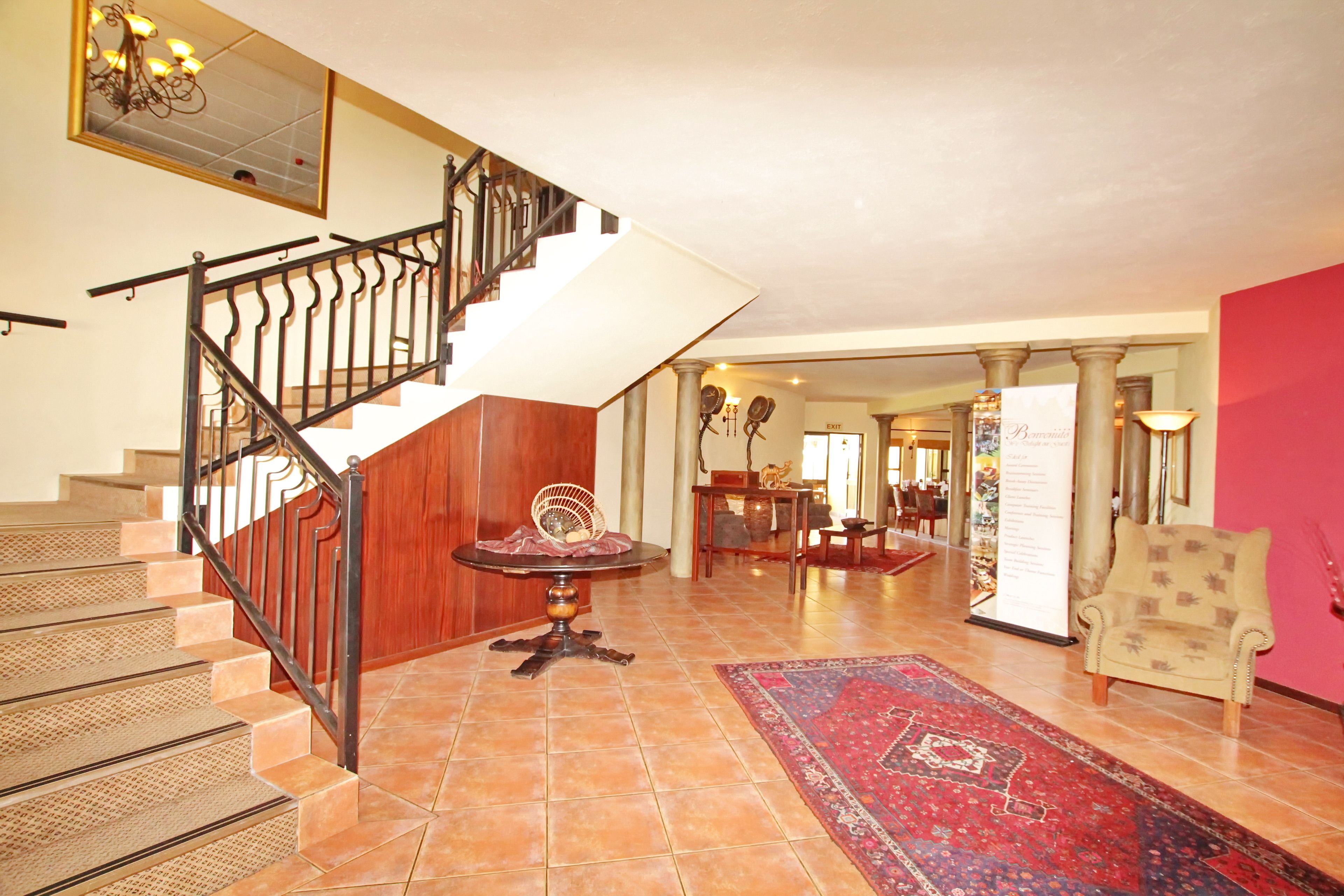 A spacious foyer with a grand staircase, a round table with a chair, and a red carpet.
