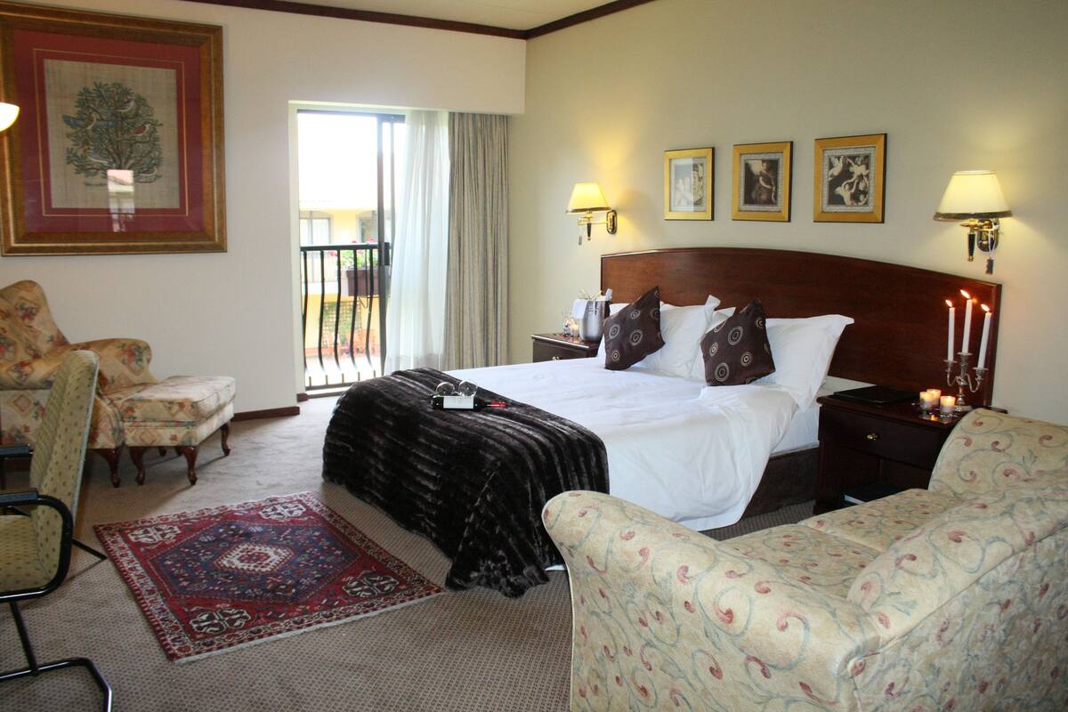 Habitación de hotel con una cama grande, dos mesitas de noche, una silla, una mesita pequeña y un tapete rojo estampado.