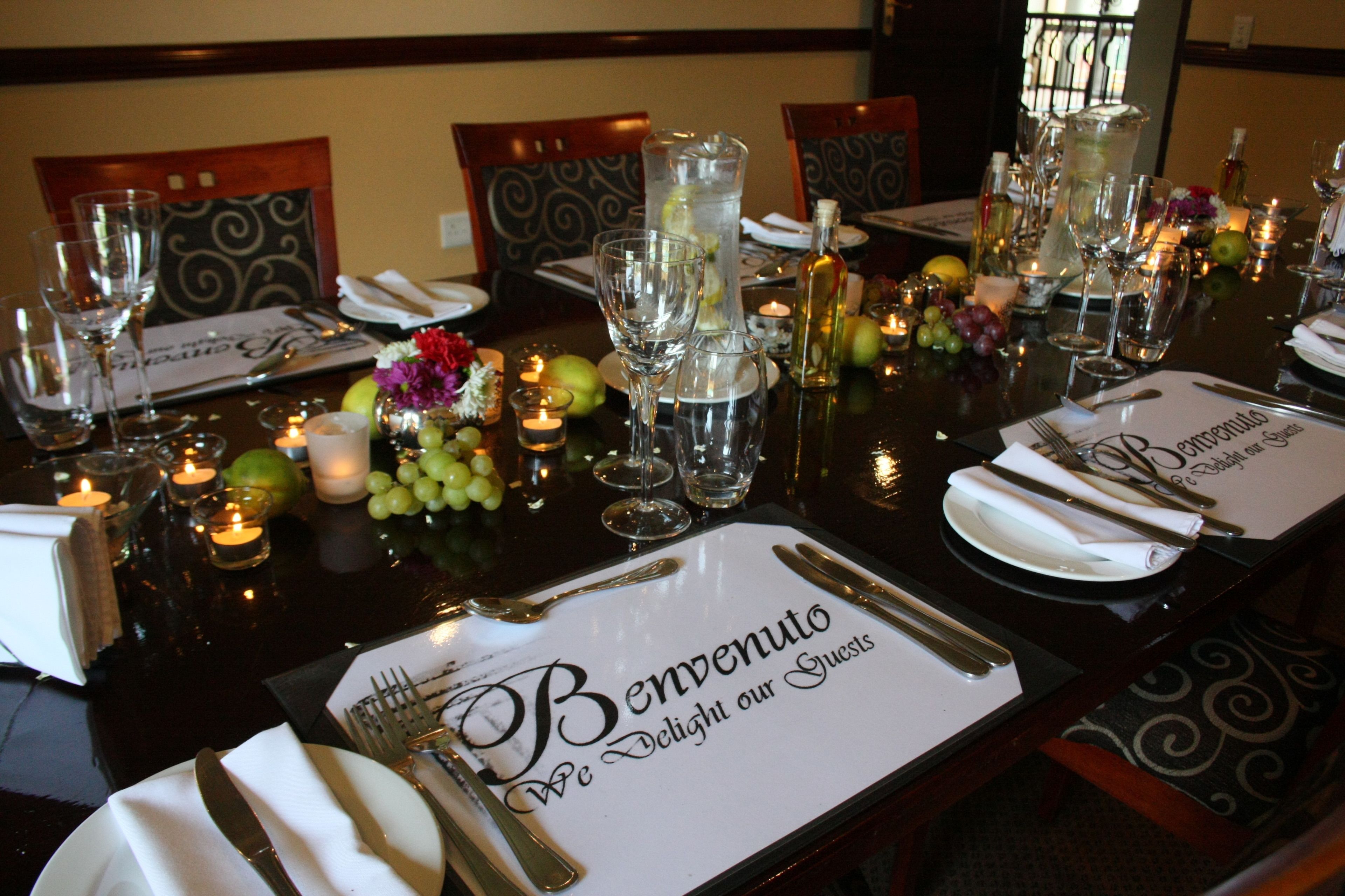 Een eettafel gedekt met wijnglazen, een karaf en kaarsen, met een menukaart waarop staat: "Benvenuto We Delight our Guests".