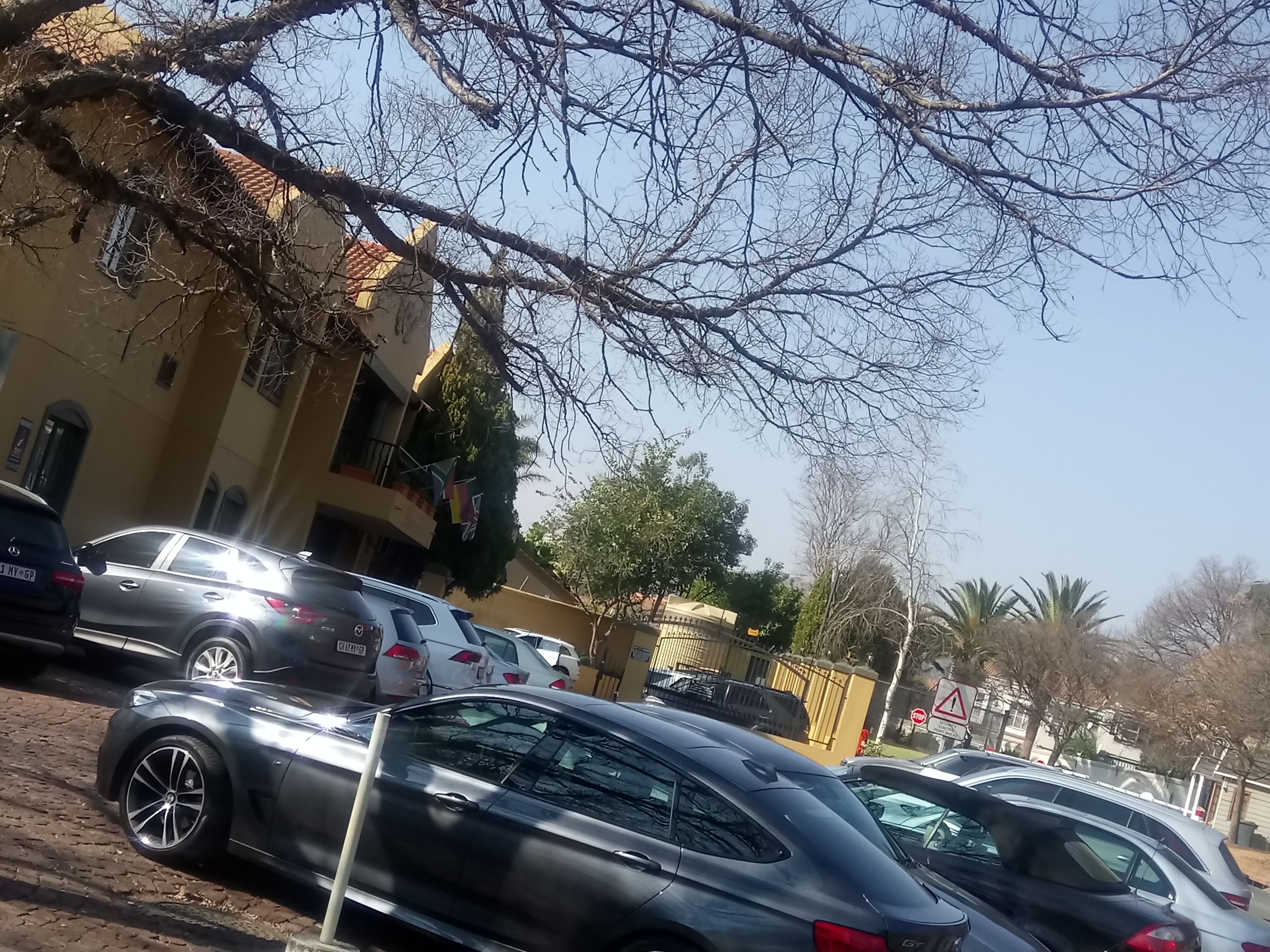 A street view with parked cars, a building with balconies, and a clear sky.