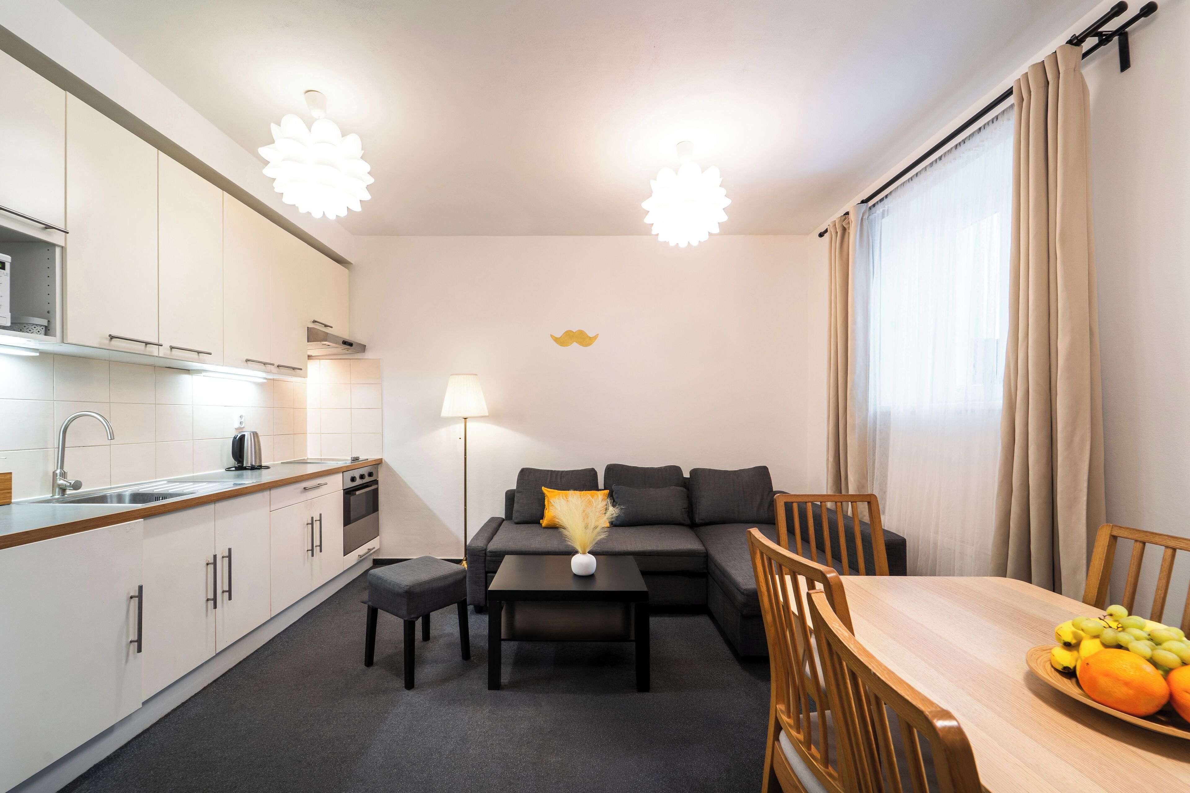 Een knus woongedeelte met een kitchenette, een bank, een eettafel en een schaal fruit.
