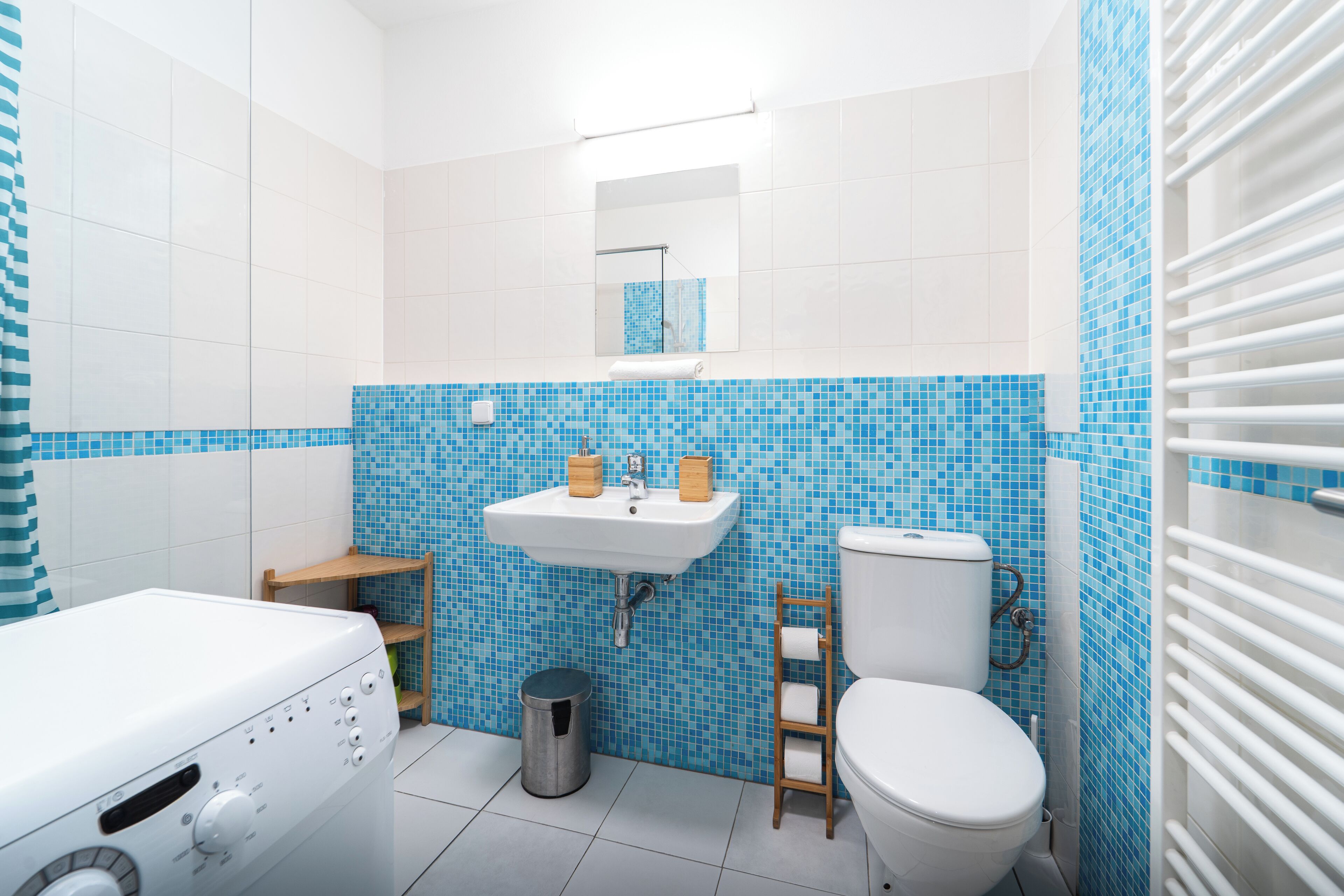 A bathroom with a white sink, blue mosaic tiles, a wooden shelf, a toilet, and a washing machine.