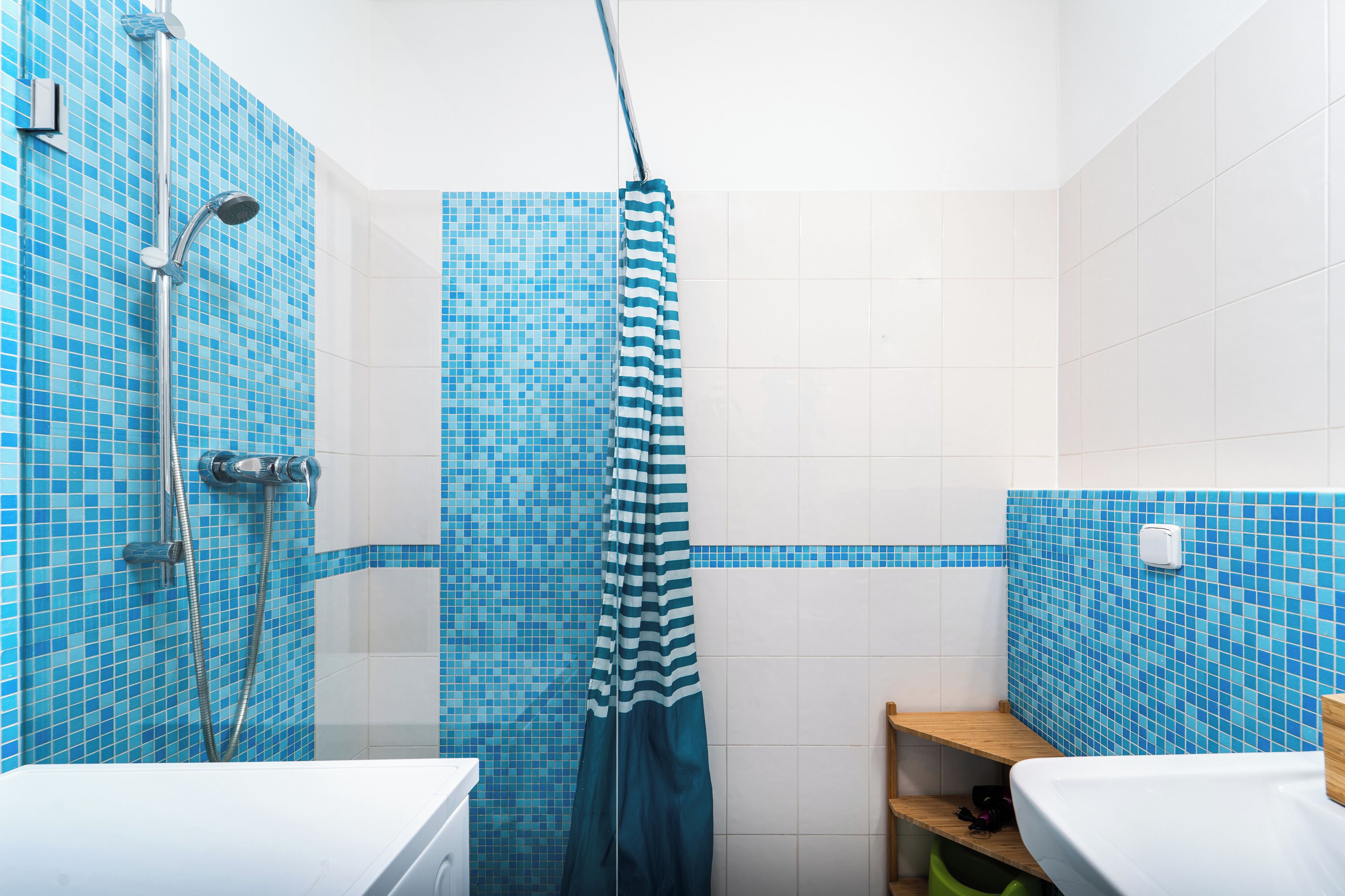 Une salle de bain avec des carreaux de mosaïque bleus, une douche avec un rideau à rayures et une étagère en bois.
