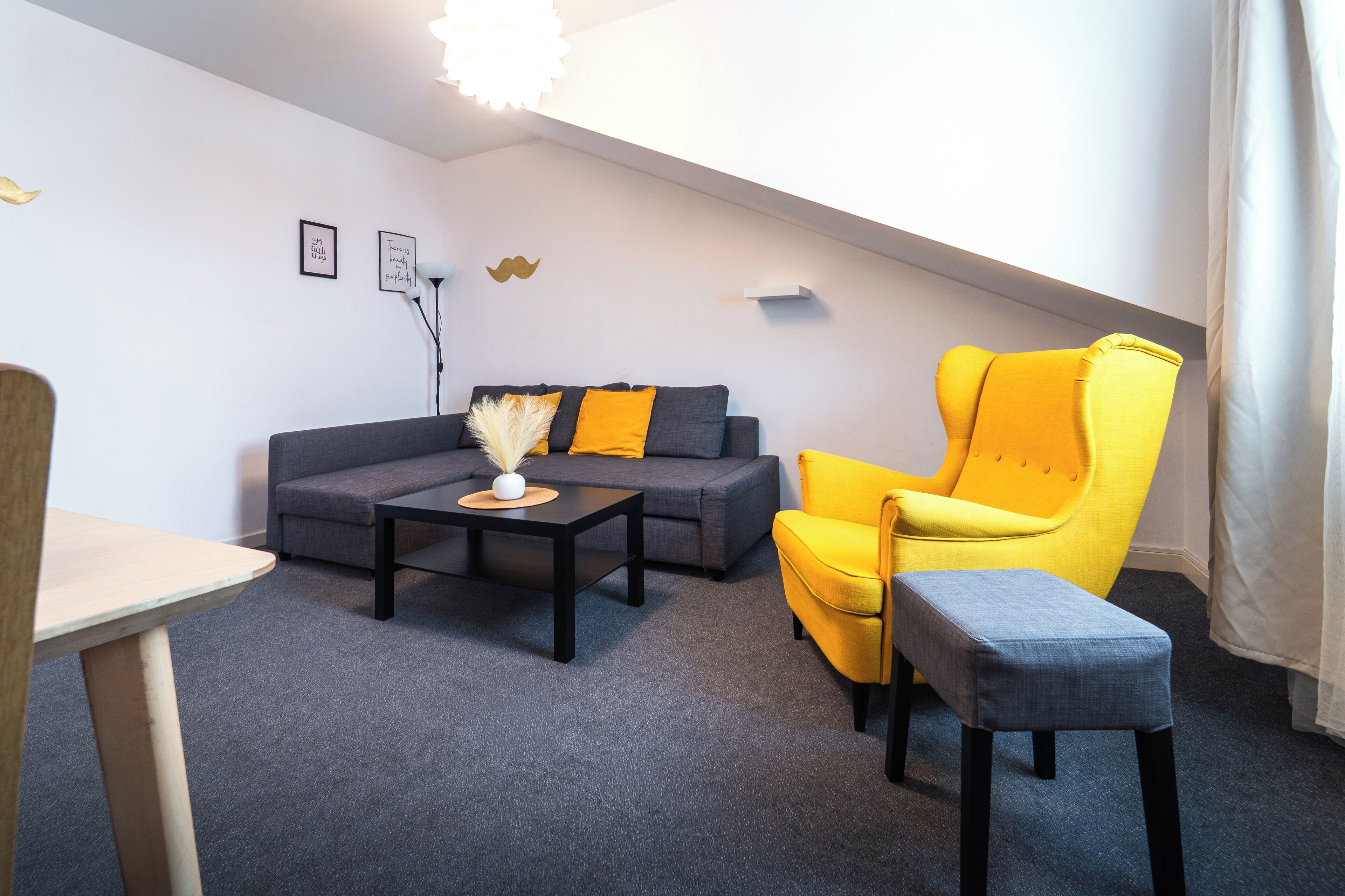 A modern living room with a grey sofa, a yellow armchair, and a small table with a vase.