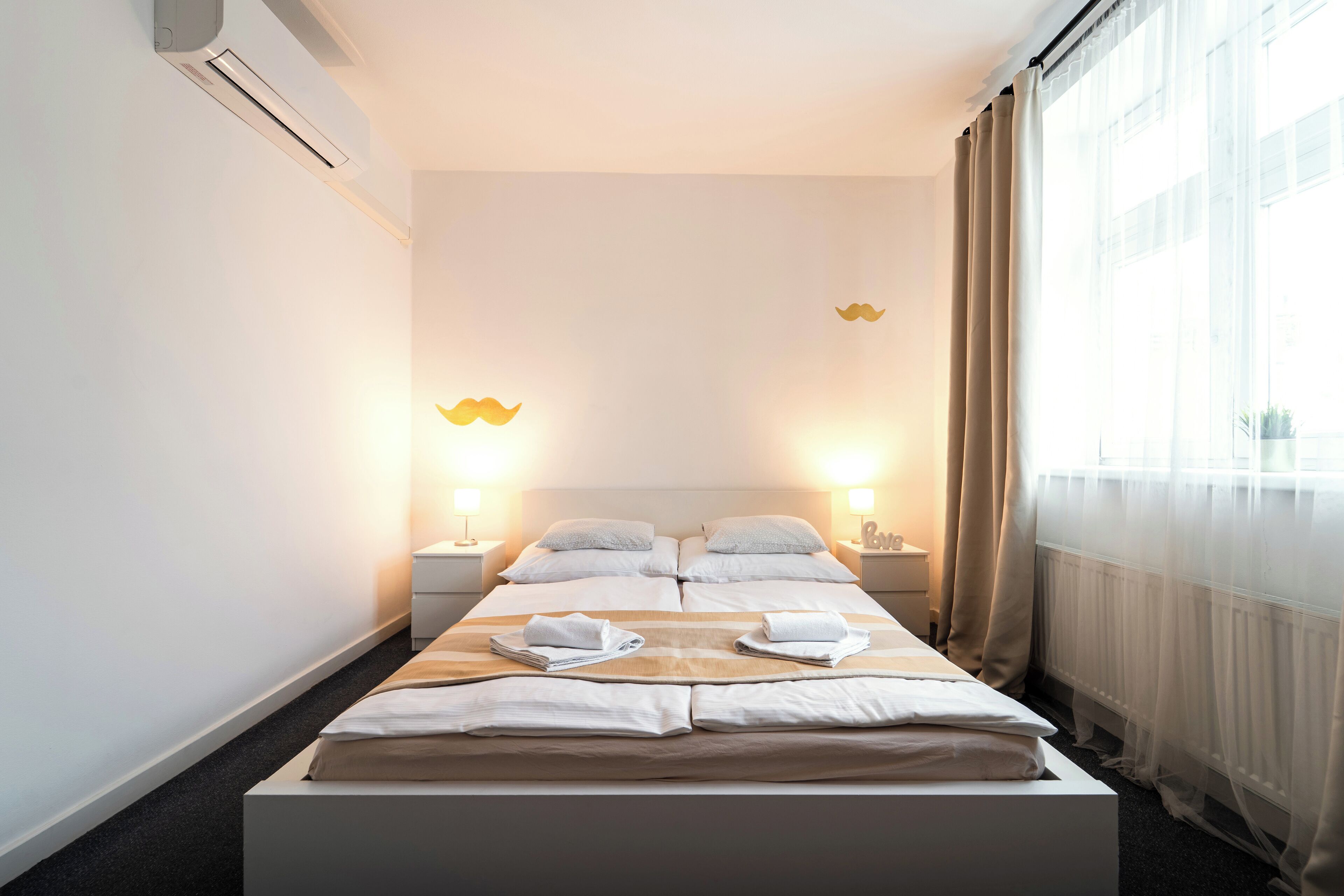 Ein Hotelzimmer mit einem großen Bett, zwei Nachttischen, einem mit Vorhängen versehenen Fenster und einer Klimaanlage.