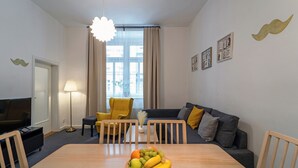 Una sala de estar moderna con una mesa de comedor, un sofá, un televisor y un ventanal con cortinas.