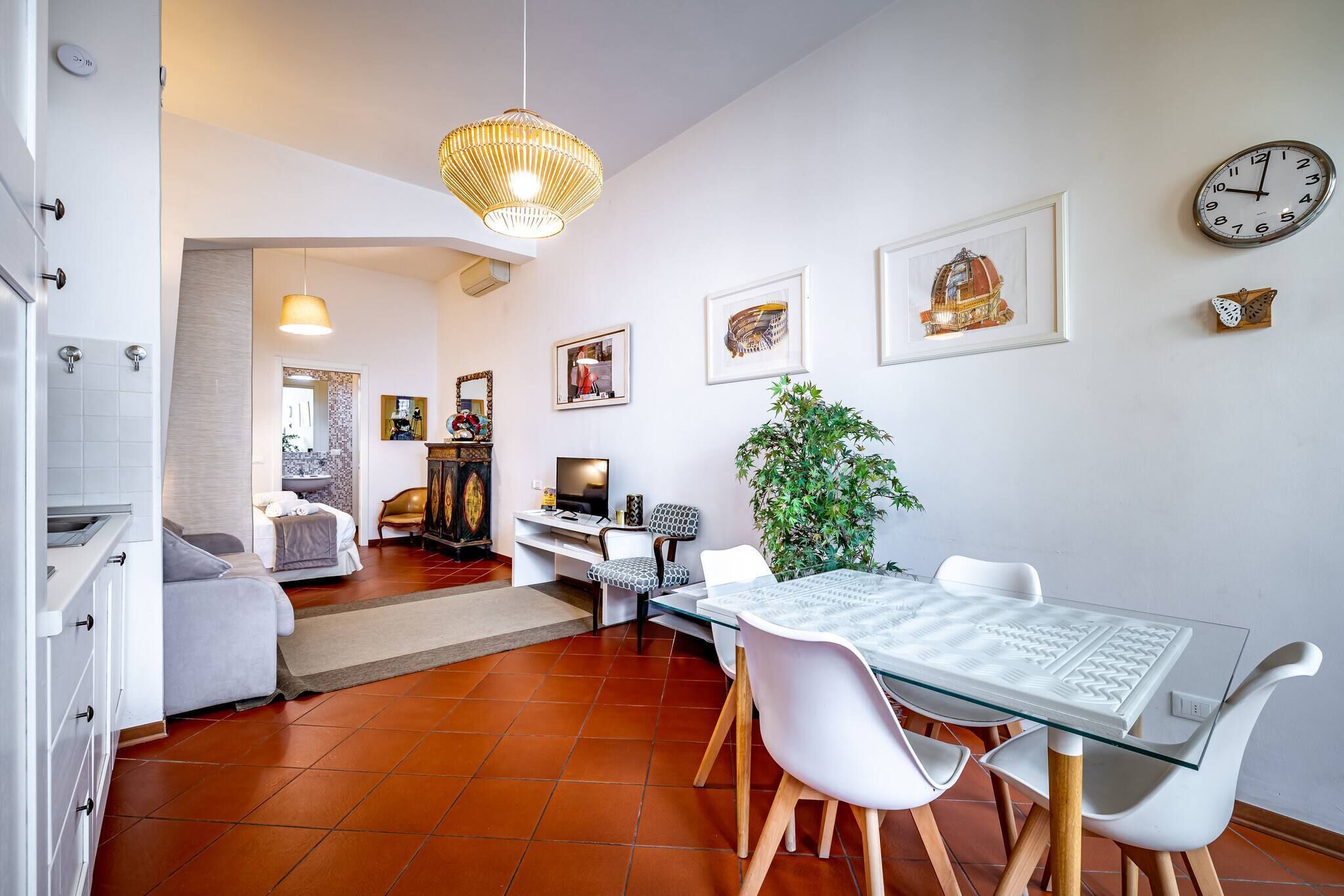 A modern kitchen with a dining area, white walls, and a clock.