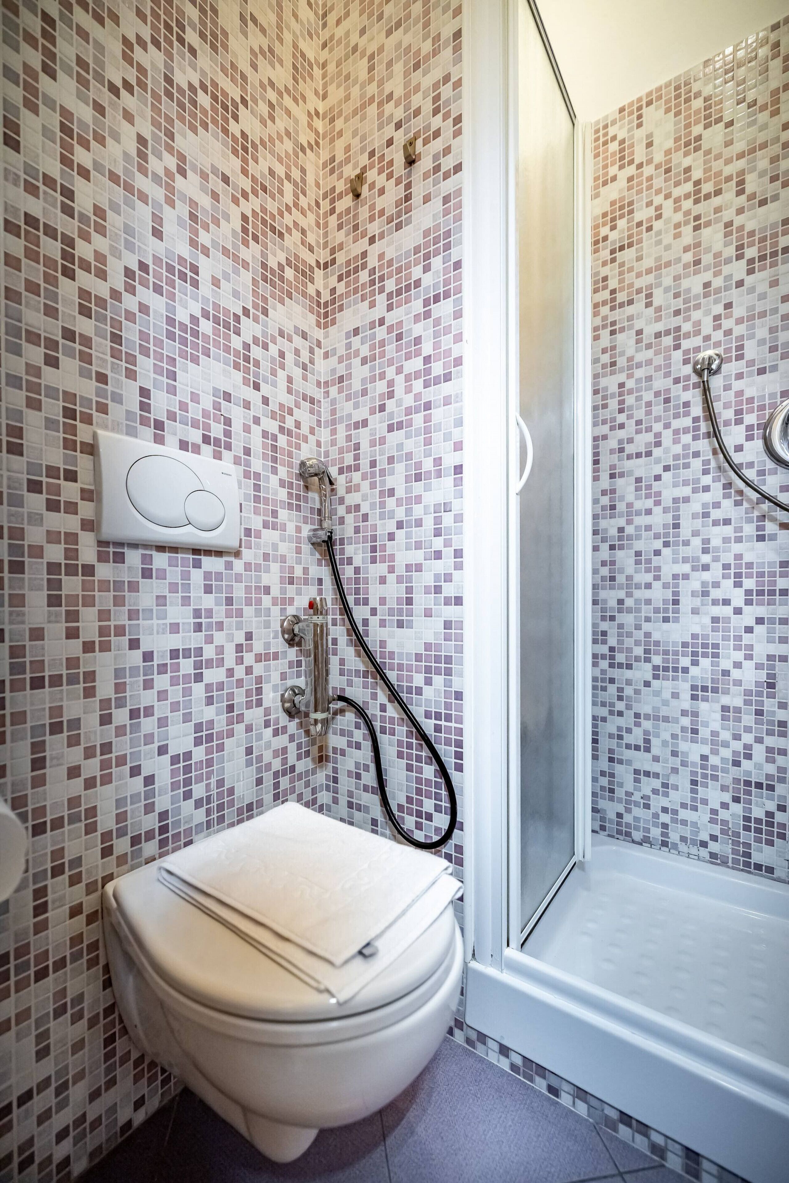 A bathroom with a toilet, a shower with a glass door, and a tiled wall.