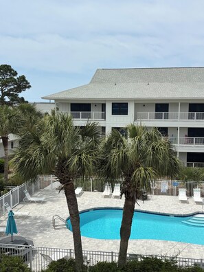 A pool area with palm trees, lounge chairs, and a two-story building with balconies. - Park your car and walk everywhere! Including the new beach access! (Santa Rosa)