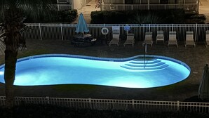 En swimmingpool med en springvand, omgivet af et hvidt hegn, samt et par liggestole.