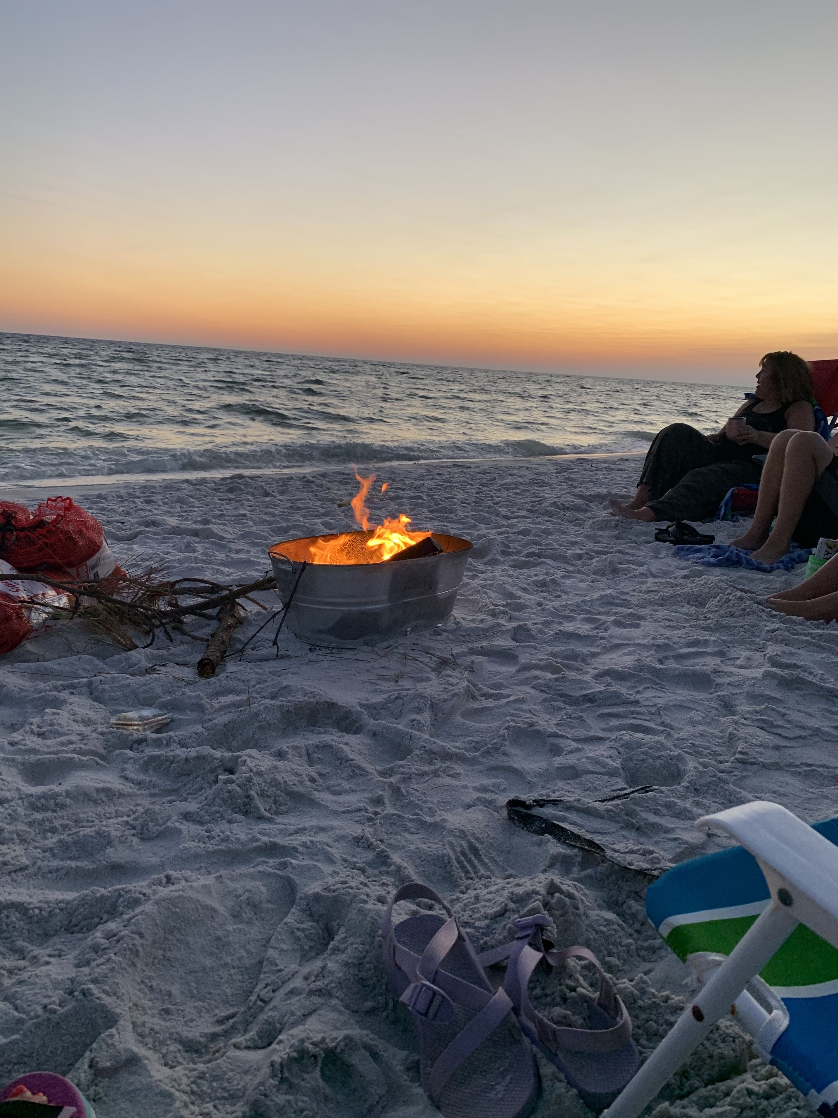 En strandscene med et lejrbål, en stol og en person, der sidder i sandet.