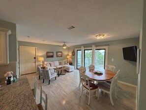 A spacious living area with a dining table, chairs, a sofa, and a television. - Park your car and walk everywhere! Including the new beach access! (Santa Rosa)