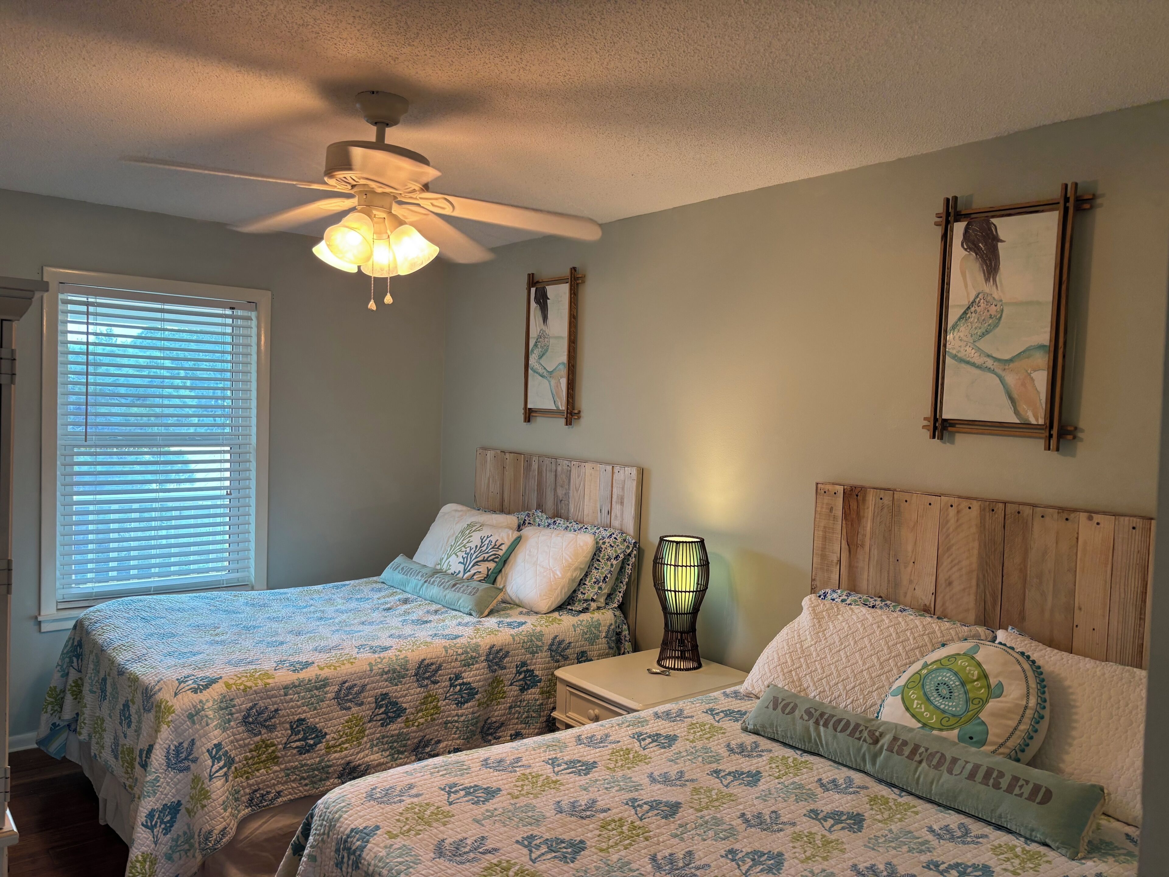 A bedroom with two beds, a ceiling fan, a nightstand, and wall art.