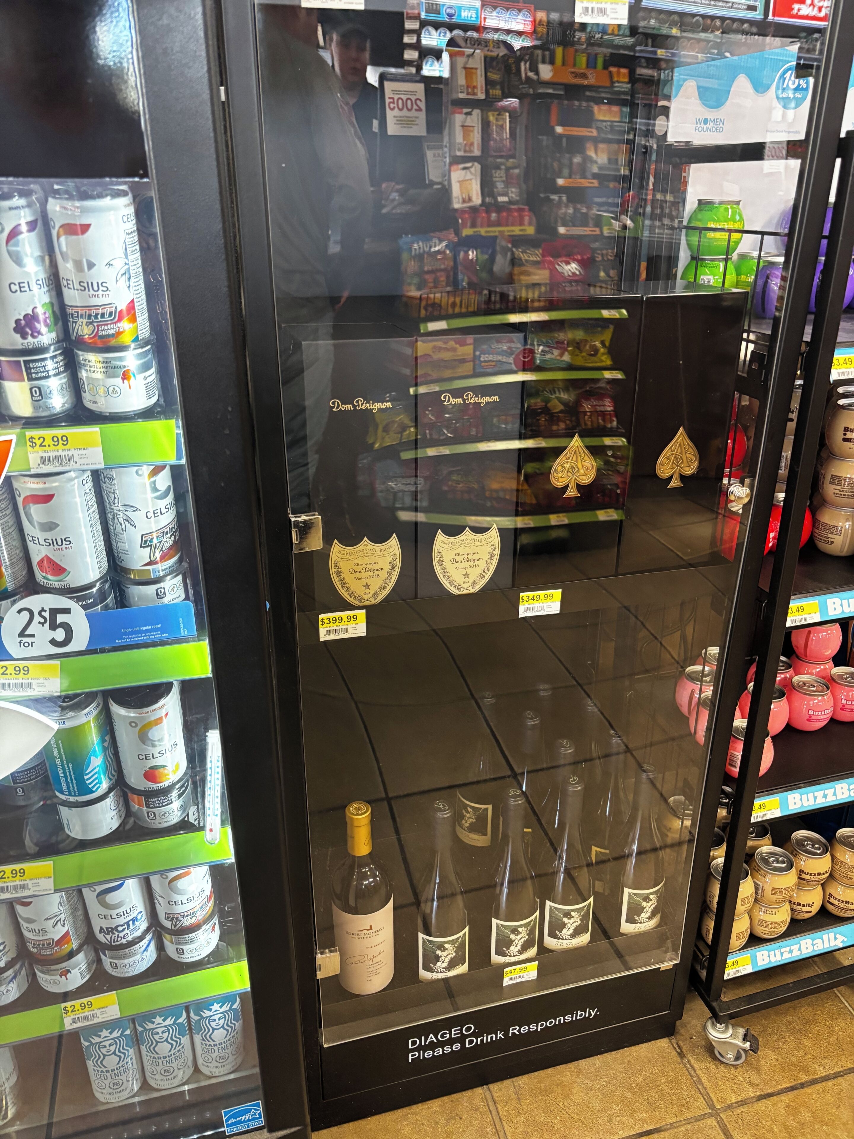 A refrigerated display case with various beverages, including energy drinks and alcoholic beverages, with price tags visible.