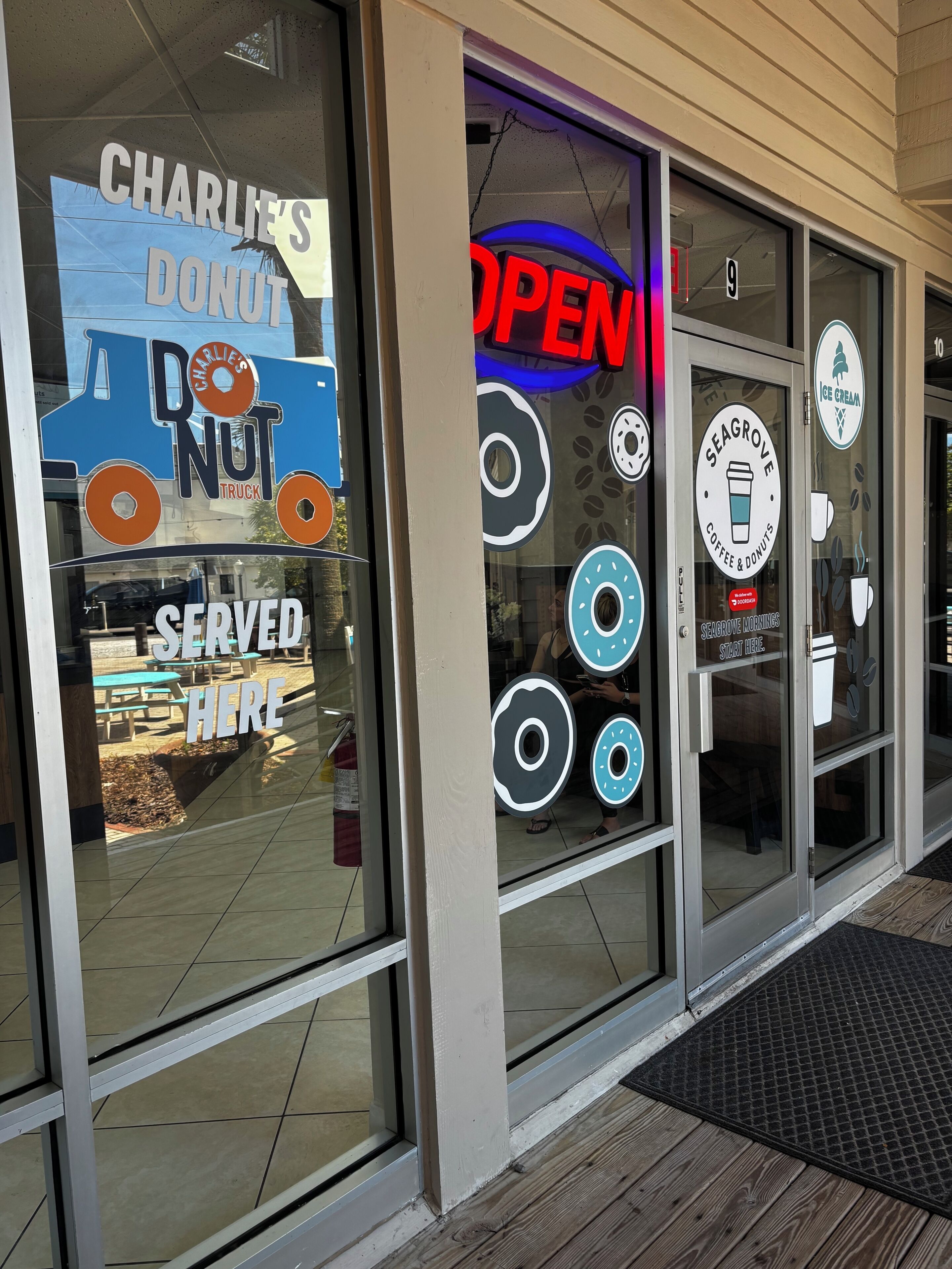 Une devanture de magasin avec une enseigne néon indiquant « OUVERT », une autre indiquant « CHARLIE'S DONUT » et une troisième indiquant « SEAGRAVE COFFEE & DONUTS ».