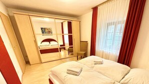 A hotel room with a large bed, a wardrobe, a chair, and a window with curtains. - Apartment Alte Fronfeste II 40sqm (Berchtesgaden)