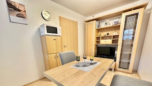 A compact living space with a wooden dining table, a microwave, a TV, and a bookshelf. - Apartment Alte Fronfeste II 40sqm (Berchtesgaden)