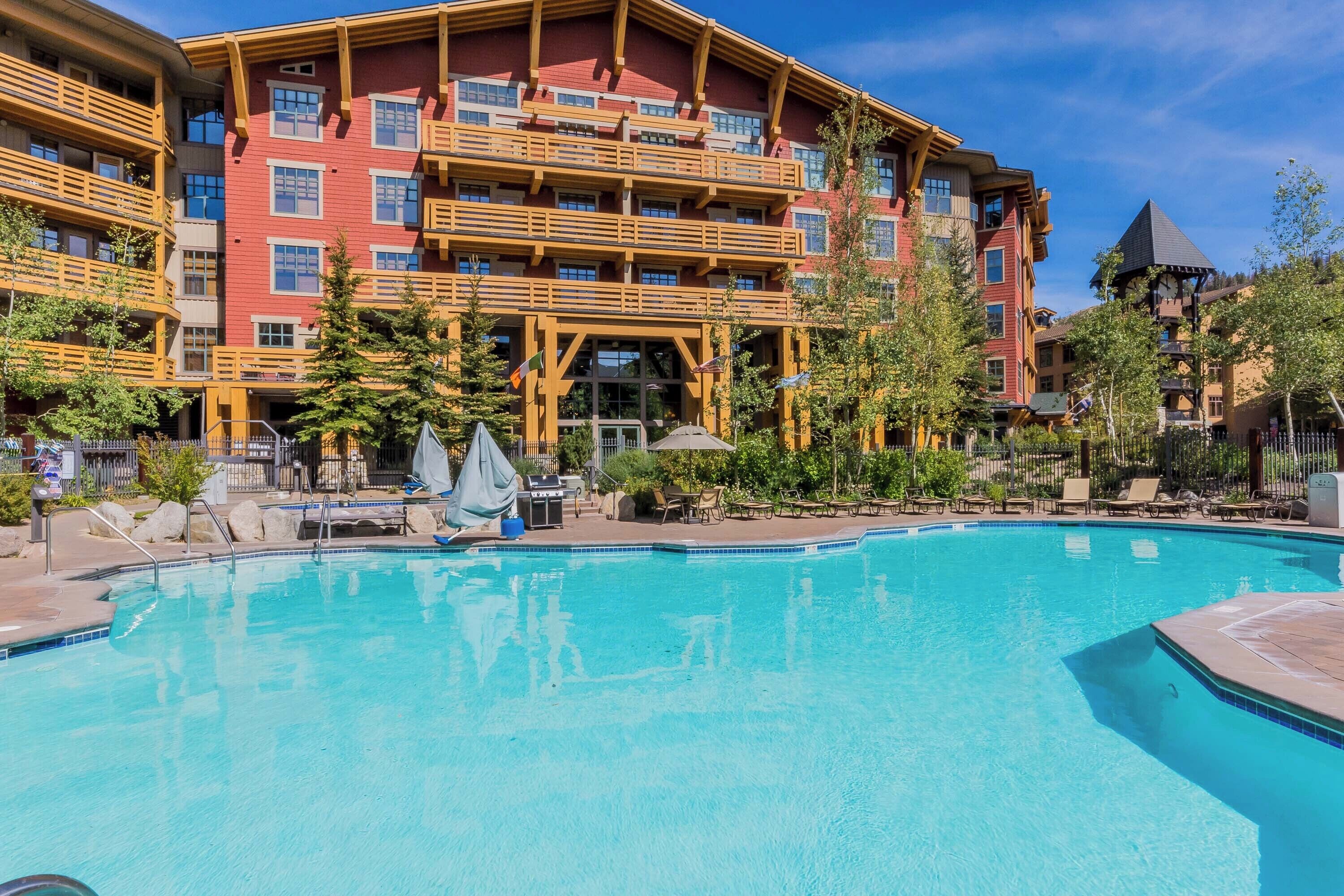A hotel with a pool, outdoor seating, and a large building with multiple balconies.