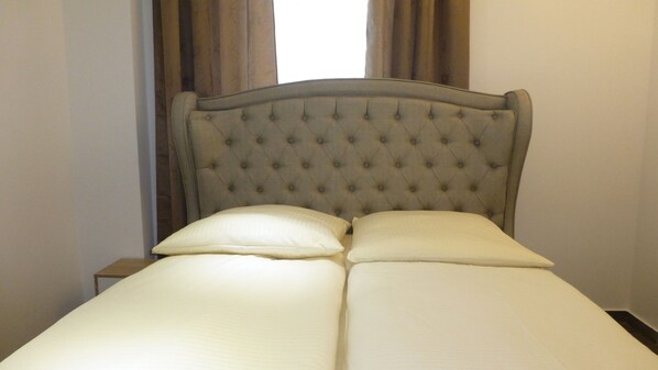 A bed with a tufted headboard, two pillows, and a wooden nightstand beside it. - HR Hotel (Hannover)