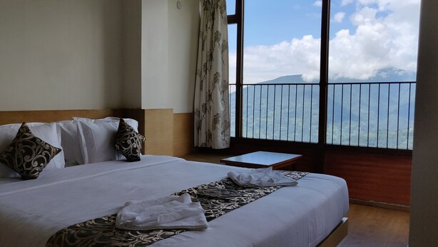 A hotel room with a large bed, a small bedside table, and a view of a mountain through a balcony railing. - Hotel Ninamma (Gangtok)
