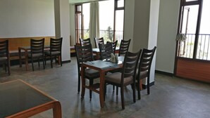 A dining area with wooden tables and chairs, large windows with curtains, and a balcony with a railing. - Hotel Ninamma (Gangtok)