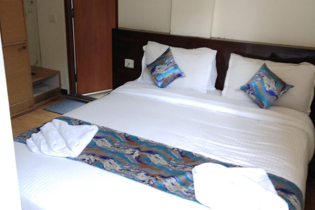 A hotel room with a bed, pillows, a wooden headboard, a white wall, and a door.