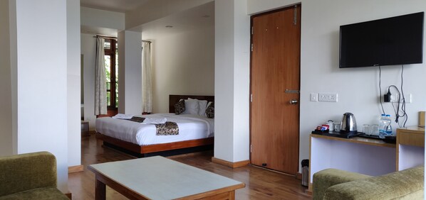 A hotel room with a bed, a TV, a desk with a kettle, and a coffee maker.