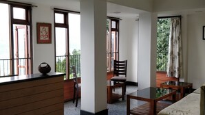 A spacious room with a reception desk, seating area, and large windows offering views of greenery. - Hotel Ninamma (Gangtok)