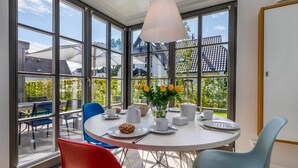 Een eetruimte met een ronde tafel, stoelen en een bloevas.