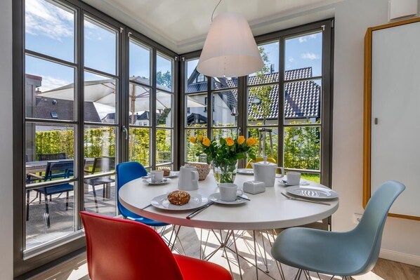 Een eetruimte met een ronde tafel, stoelen en een bloevas.