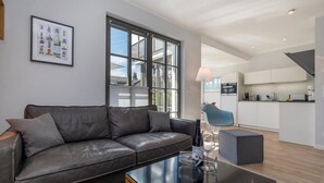 Een moderne woonkamer met een leren bank, een glazen salontafel en een keuken op de achtergrond.