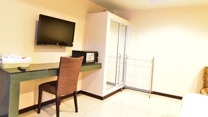 A hotel room with a desk, chair, television, and a sliding glass door leading to a balcony. - Joy House (Pattaya)