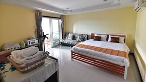 A hotel room with a bed, a sofa, a microwave, and a window with curtains. - Joy House (Pattaya)