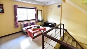 A room with a sofa, a table with a plant, a window with curtains, a fan, and a staircase. - Joy House (Pattaya)