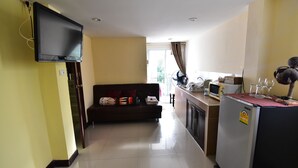 A living room with a flat-screen TV, a sofa with cushions, a kitchen area with a refrigerator, and a dining table. - Joy House (Pattaya)