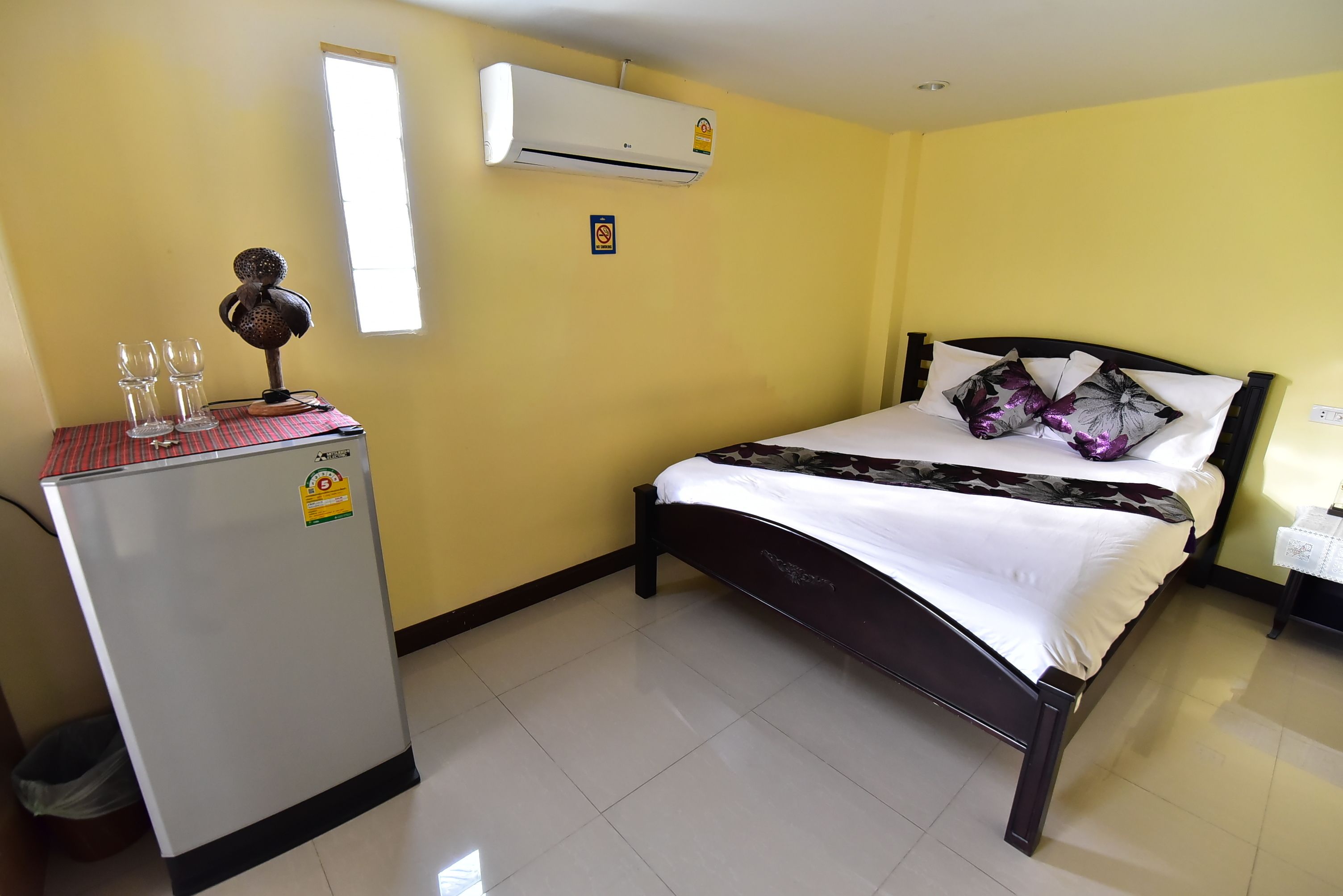 A hotel room with a bed, a small refrigerator, and an air conditioner.