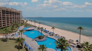Een resort met meerdere zwembaden, een strand en een groot hotelgebouw.