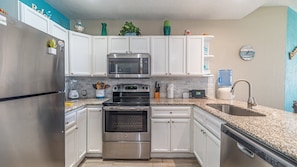 Fully equipped kitchen with stainless steel appliances, white cabinetry, and granite countertop.