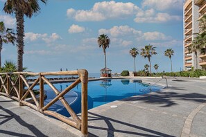 Relax by the resort pool surrounded by palm trees and a wooden fence.