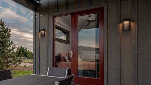 Un edificio moderno con puerta corredera de vidrio que da a un dormitorio con cama y ventilador de techo. Cuenta con un patio con mesa y sillas.
