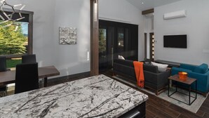 Una sala moderna con una isla de cocina de mármol, un sofá negro, un sillón azul y un televisor de pantalla plana montado en la pared.