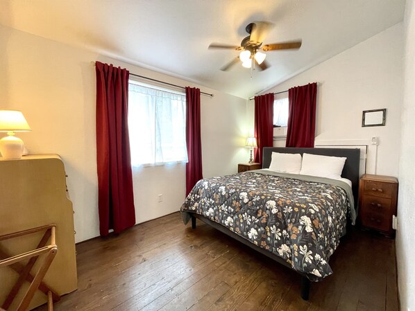 A bedroom with a bed, a ceiling fan, a nightstand, a lamp, and a window with curtains.