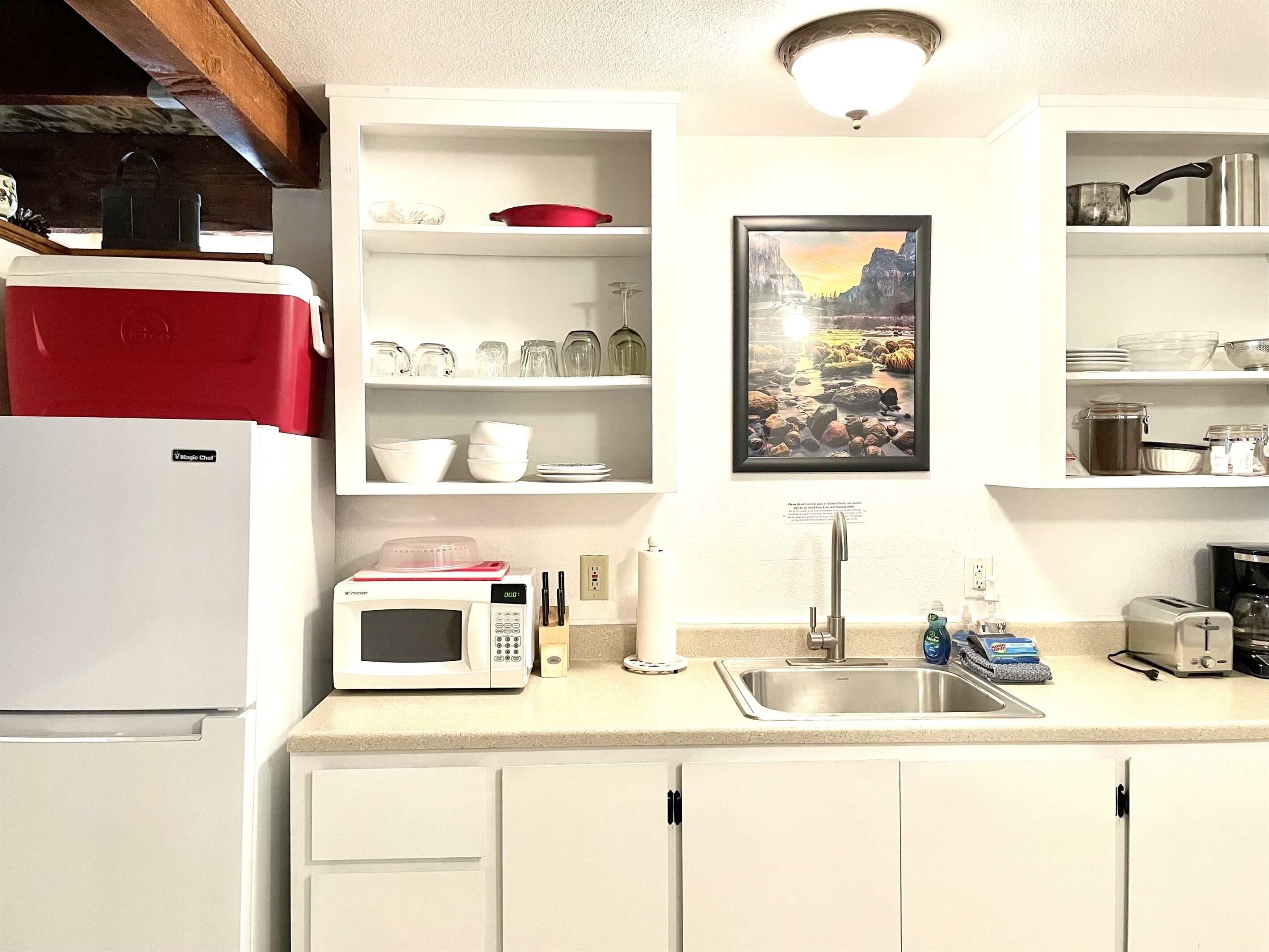 A kitchen with white cabinets, a microwave, a sink, and a framed picture on the wall.