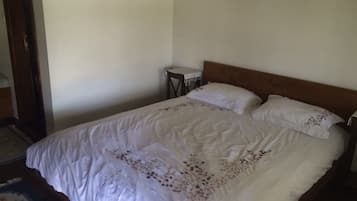 A bedroom with a large bed, a small bedside table, and a wall-mounted light fixture.