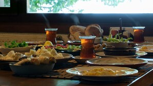 Uma mesa com diversos pratos e bebidas, incluindo uma tigela de queijo, um prato de ovos mexidos e copos de chá.