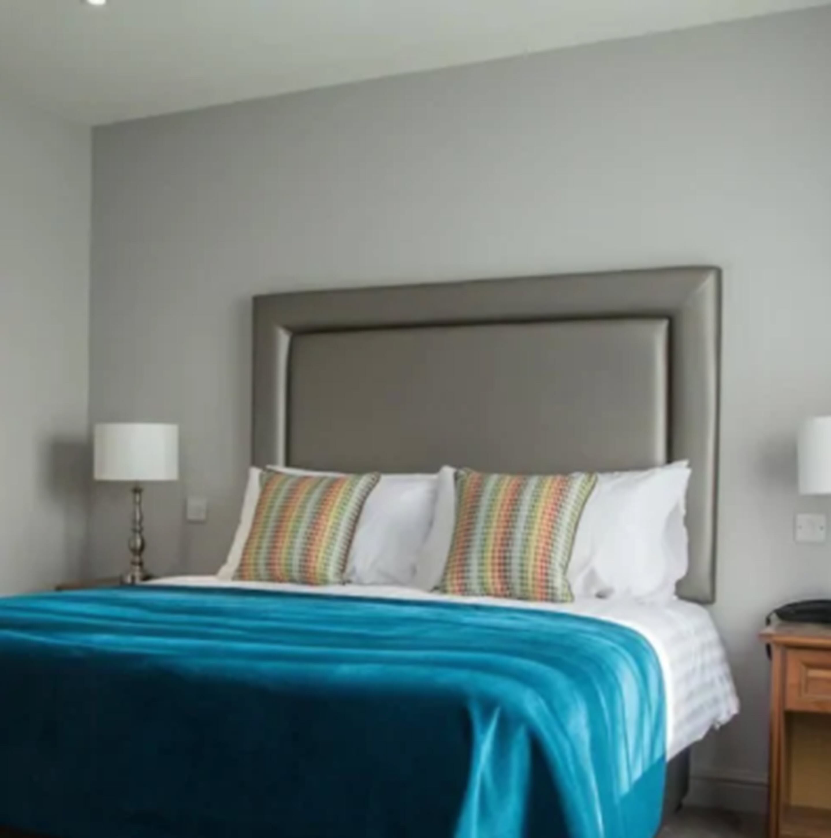 Habitación de hotel con una cama grande, un cabecero y una mesita de noche con una lámpara.