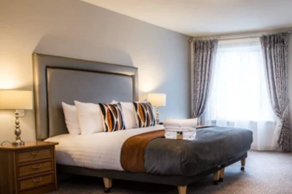 A hotel room with a large bed, a nightstand, a lamp, and a window with curtains.