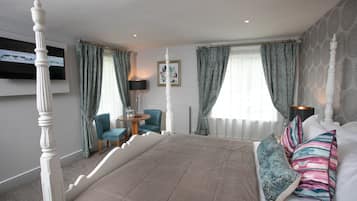 A bedroom with a four-poster bed, a round table with a chair, and a framed picture on the wall.